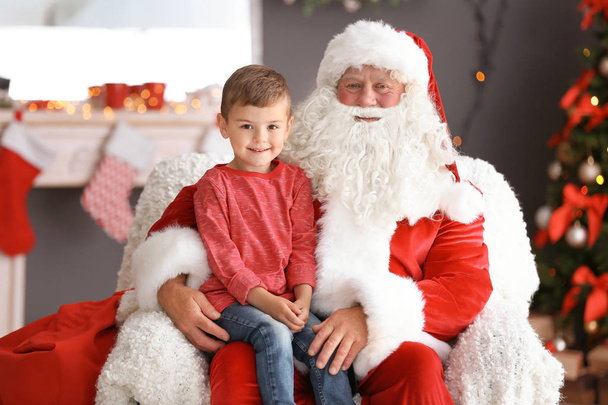 Little boy sitting on authentic Santa Claus' lap indoors - Foto, afbeelding