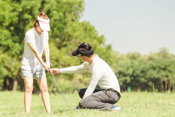 asiatisches Paar beim Golfspielen. Mann lehrt Frau Golf spielen, während sie auf dem Feld steht - Foto, Bild