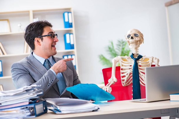 Uomo d'affari che lavora con scheletro in ufficio - Foto, immagini