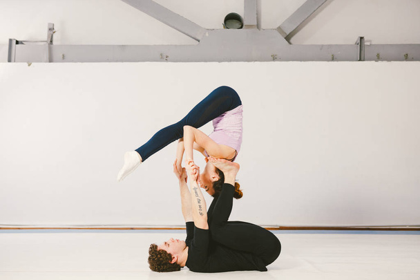 Una joven pareja caucásica de hombres y mujeres practicando yoga acrobático en un gimnasio blanco sobre esteras. Están en la pose STAR
. - Foto, imagen