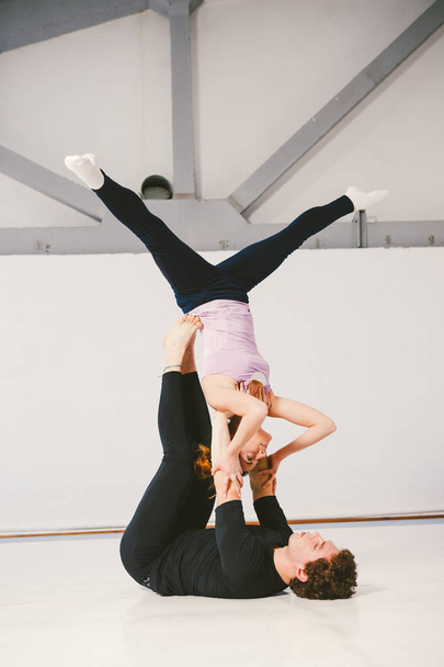 ein junges kaukasisches Paar, das akrobatisches Yoga in einer weißen Turnhalle auf Matten praktiziert. Sie sind in der Sternenpose. - Foto, Bild