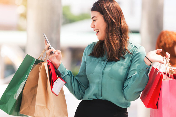 Hermosas chicas en la ciudad sosteniendo bolsas de compras, utilizando un teléfono inteligente jugando compras en línea
 - Foto, imagen