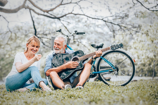 Senior couple in love playing acoustic song  guitar sitting on grass in the park - Fotoğraf, Görsel