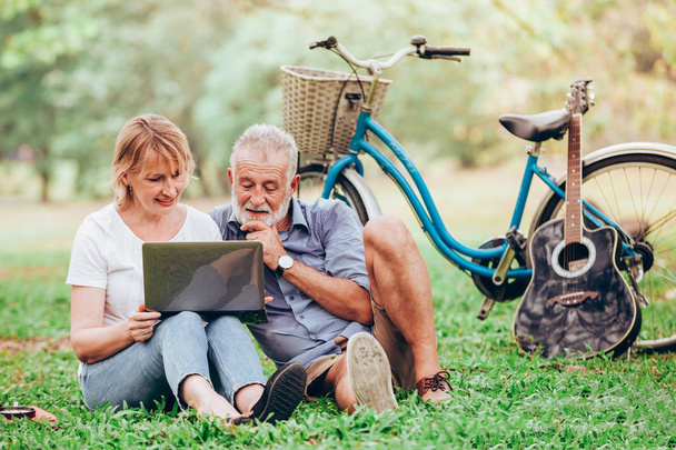 Vanhempi pari käyttää kannettavaa tietokonetta istuessaan nurmikolla puistossa
 - Valokuva, kuva