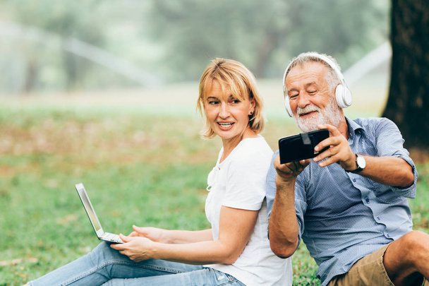 Старшая пара любит слушать музыку, сидя на траве в парке
 - Фото, изображение