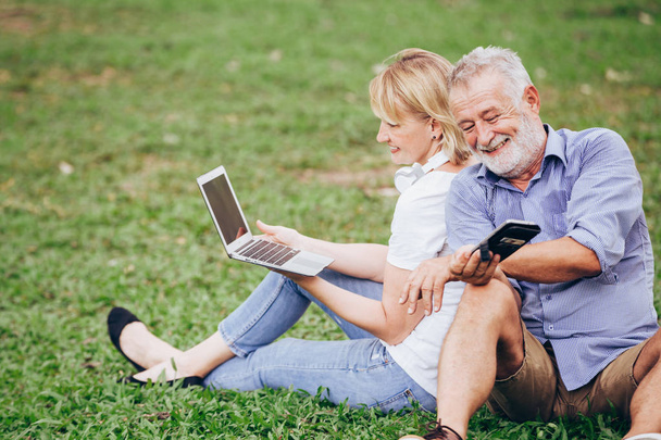 Senior couple enjoy listening to music while sitting on grass in the park - Foto, imagen