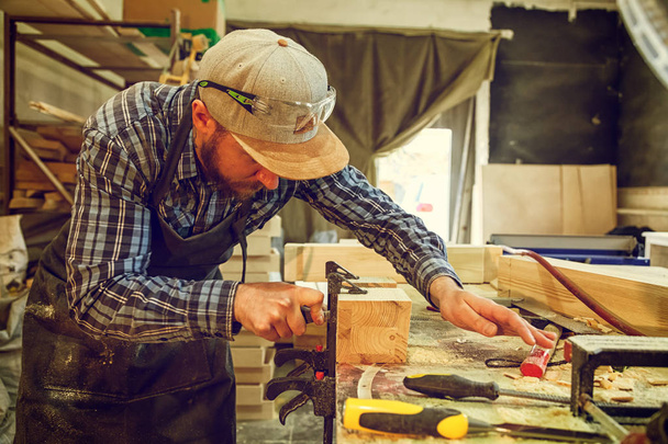 Ισχυρή ξυλουργός με ρούχα εργασίας σκάλισμα ξύλο χρησιμοποιώντας ένα εργαλείο επεξεργασίας ξύλου, σμίλη, χέρια εσωτερικη, ξυλουργική και δεξιοτεχνία έννοια - Φωτογραφία, εικόνα