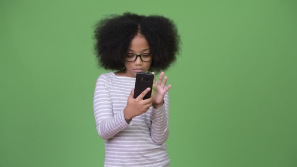 Young cute African girl with Afro hair looking shocked while using phone - Záběry, video