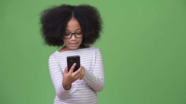 Young cute African girl with Afro hair using phone and celebrating - Metraje, vídeo