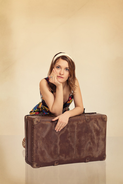 Beautiful girl leaning on old suitcase toned in retro style - Фото, изображение