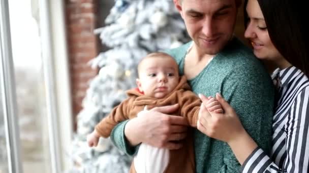 νεαρή οικογένεια με ένα παιδί σε ένα φόντο από μια Χριστουγεννιάτικη διακόσμηση - Πλάνα, βίντεο