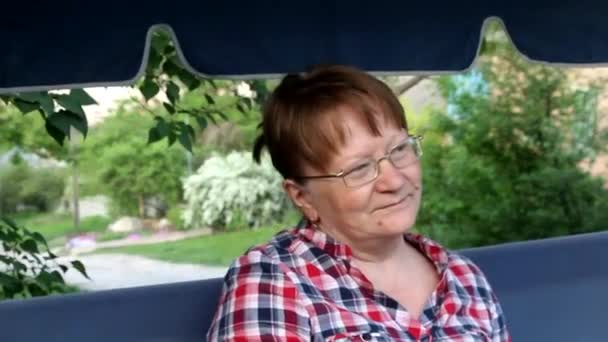 mulher de meia-idade sentado em um balanço de jardim e olhando atenciosamente para a distância
 - Filmagem, Vídeo