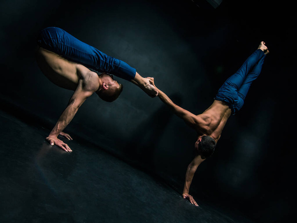 Male acrobatic duo performs a complicated balancing act on a dark background. - Photo, image