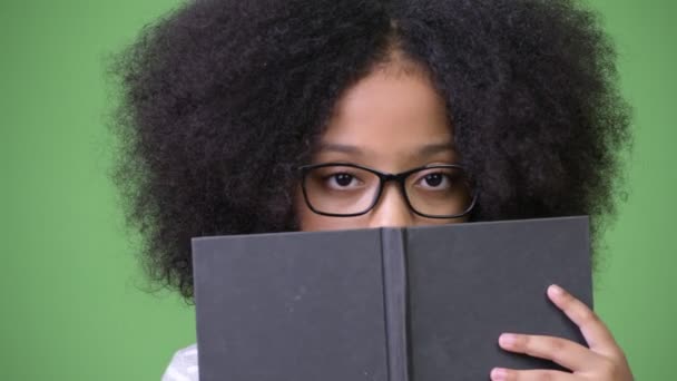Young cute African girl with Afro hair studying against green background - Imágenes, Vídeo