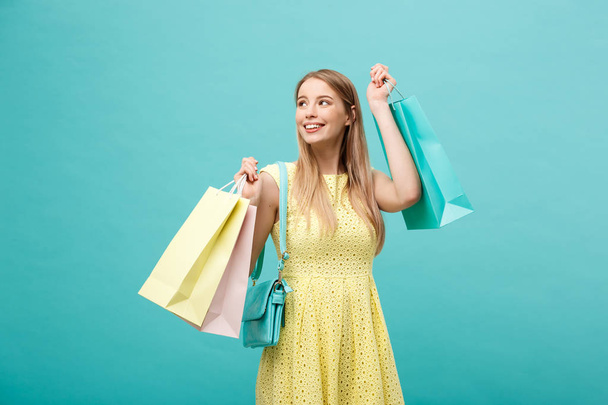 Shopping Concept: Portrait of an excited beautiful girl wearing yellow dress holding shopping bags isolated over blue background - Foto, immagini