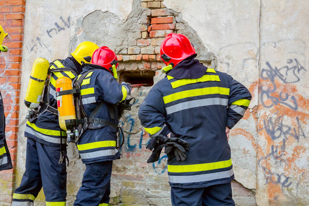 Van achteren kijk op brandweerman in uniform met volledige veiligheid vistuig, met behulp van Koevoet te breken bakstenen muur.  - Foto, afbeelding