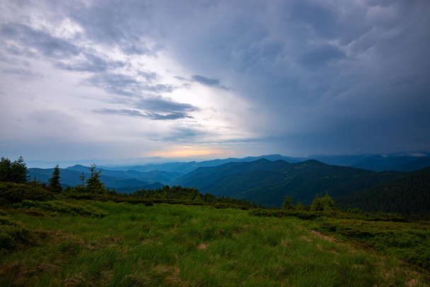 Tolle Berglandschaft vor dem Sturm - schwere graue Wolken schweben über den grünen bewaldeten Hügeln bis zum Horizont bei Sonnenuntergang. Weitwinkel. - Foto, Bild