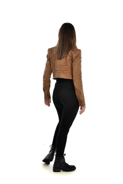 ritratto a figura intera di ragazza bruna che indossa giacca di pelle e vestiti neri. posa in piedi, isolato su sfondo bianco studio
. - Foto, immagini