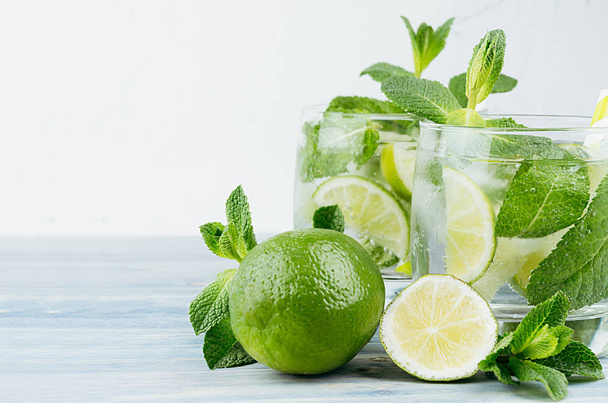 Summer cool lemonade in two wet glasses with mint, lime, ice, straw on vintage white plaster background, copy space, closeup. - Foto, imagen