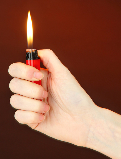 Burning lighter in female hand, on dark brown background - 写真・画像