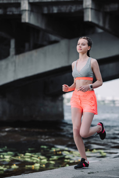 beautiful sportswoman with smartwatch running on quay - 写真・画像