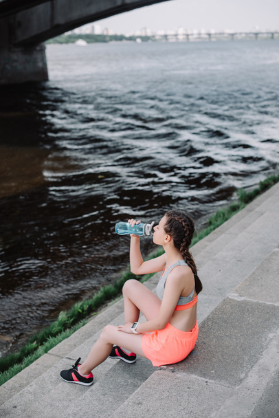 fille sportive boire de l'eau de bouteille de sport tout en étant assis sur le quai près de la rivière
 - Photo, image