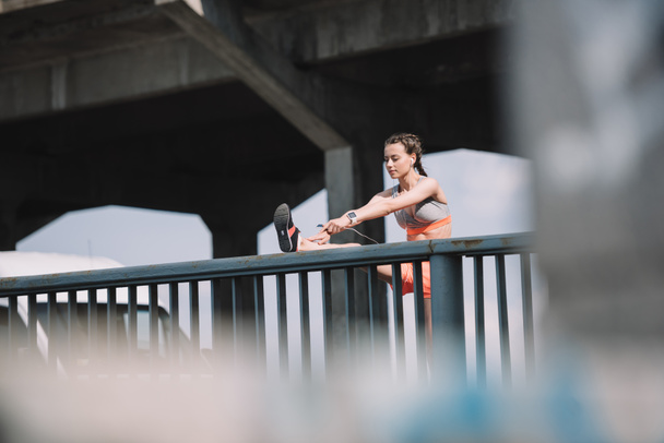 спортивна дівчина розтягує ногу на перилах на мосту
 - Фото, зображення