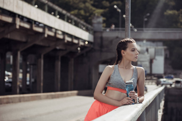 attractive sportswoman holding sports bottle with water in city - 写真・画像