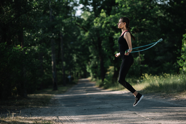 attractive sportive woman training with jump rope on path in park - Zdjęcie, obraz