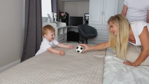Tata i Mama grać z chłopcem na łóżku z piłką - Materiał filmowy, wideo