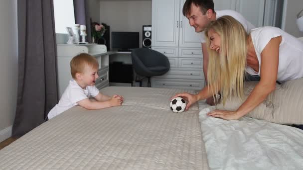 Dad and mom play with the boy on the bed with the ball - Footage, Video
