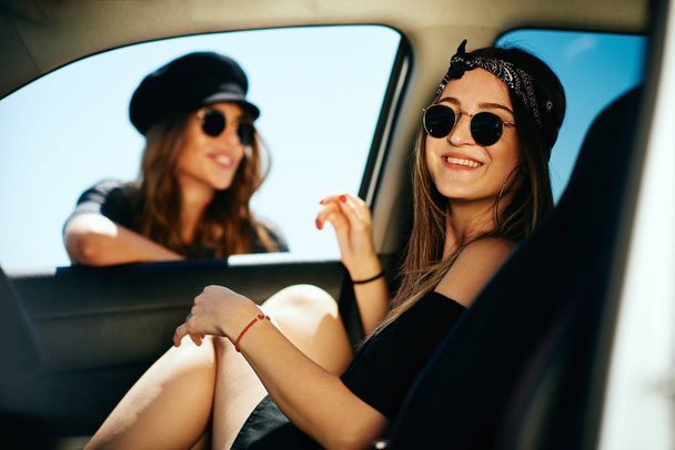 Twee vrouwen nemen van een pauze van de rijbevoegdheid. Een vrouw in de auto en andere leunend op de autoruit. - Foto, afbeelding