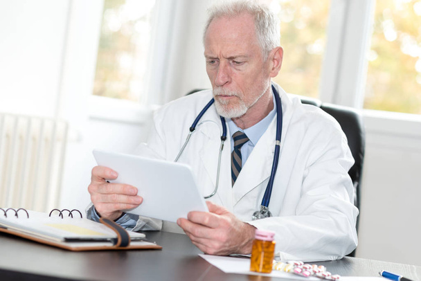 Médico senior usando tableta en el consultorio
 - Foto, imagen