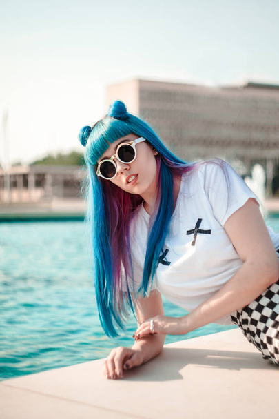 Portrait of young woman with blue hair wearing sunglasses posing at pool - Valokuva, kuva