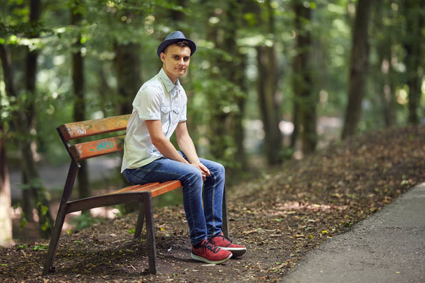 Happy handsome young man sitting on a bench in the park - Фото, изображение