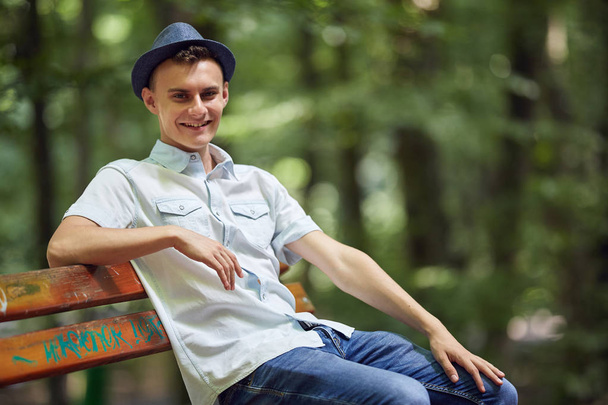 Happy handsome young man sitting on a bench in the park - Foto, Imagen