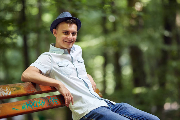 Happy handsome young man sitting on a bench in the park - Foto, imagen
