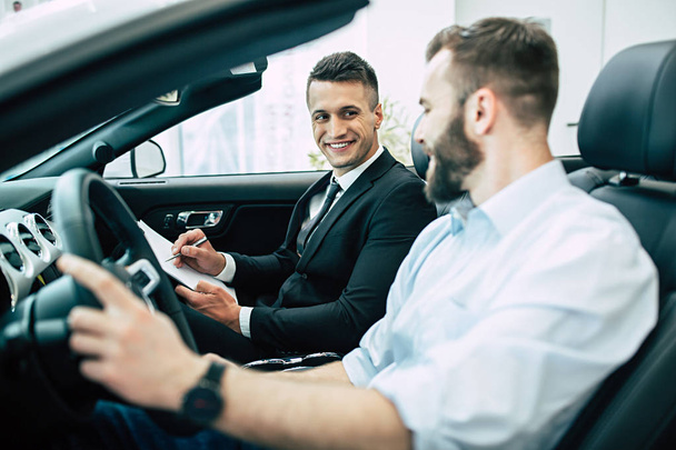 Bearded man buying new cabriolet at dealership, salesman sitting with documents - Foto, immagini