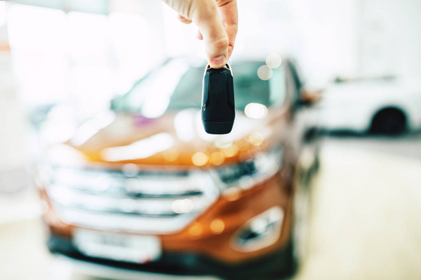 Male hand holding car keys. View of row new car at dealership indoors - 写真・画像