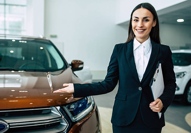 smiling businesswoman in black suit holding documents showing cars  - Foto, imagen