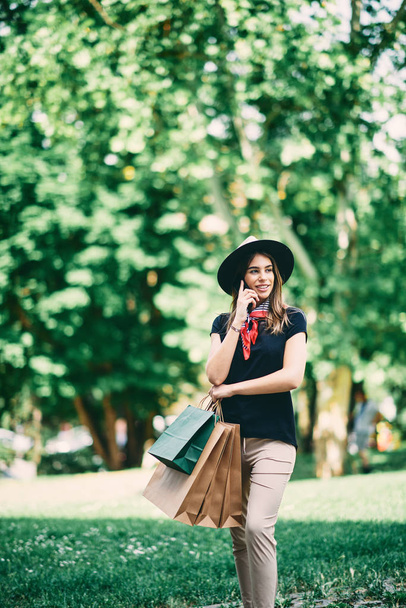Retrato de mujer usando teléfono inteligente y de pie en el parque después de ir de compras
. - Foto, Imagen
