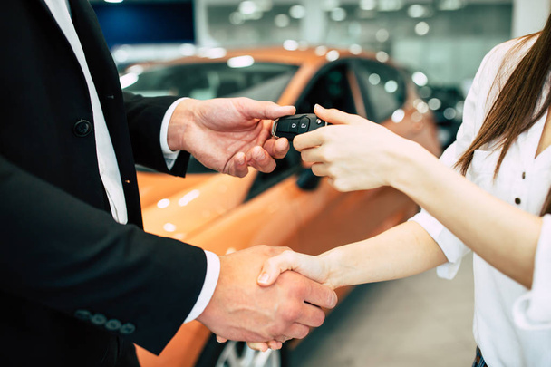 woman  receiving key of new car from salesman in dealership, close up of hands - Foto, afbeelding