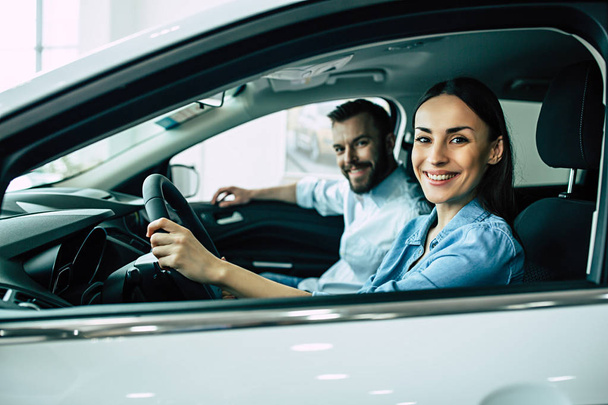 happy couple sitting in new car in dealership, choosing car concept - Фото, зображення