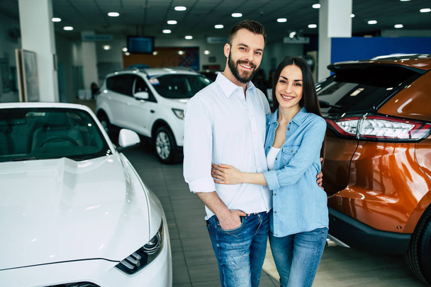 Happy couple hugging standing on car background in dealership - Fotó, kép