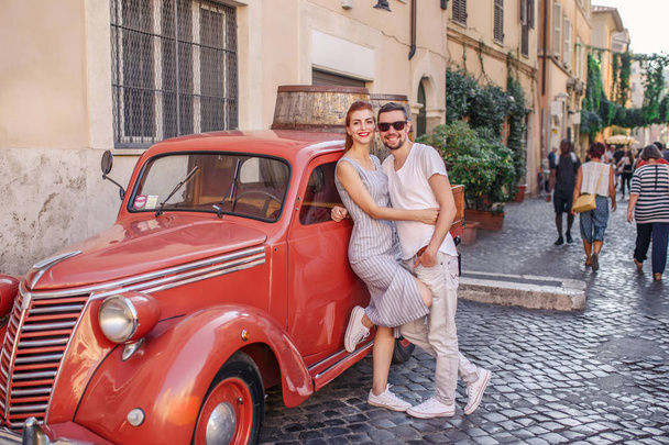 Young couple posing near red vintage car on cobbled street - Fotó, kép