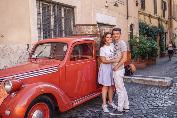 Young couple posing near red vintage car on cobbled street - Фото, изображение