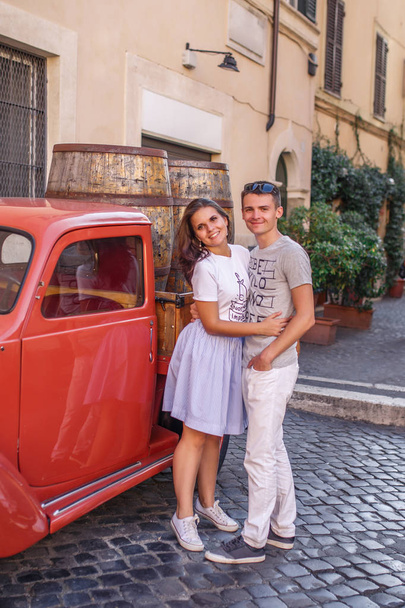 Young couple posing near red vintage car on cobbled street - Fotografie, Obrázek