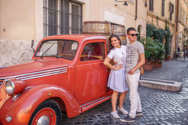 Young couple posing near red vintage car on cobbled street - Fotó, kép