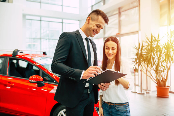 woman buying new car in dealership talking to male consultant with documents - 写真・画像
