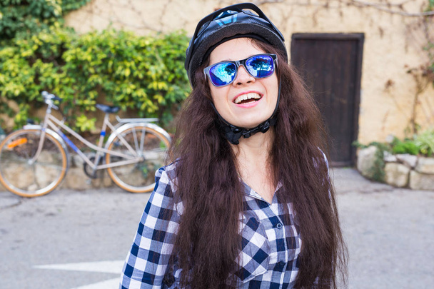 Donna sorridente con casco e occhiali da sole posizione su sfondo bicicletta e vicolo
 - Foto, immagini